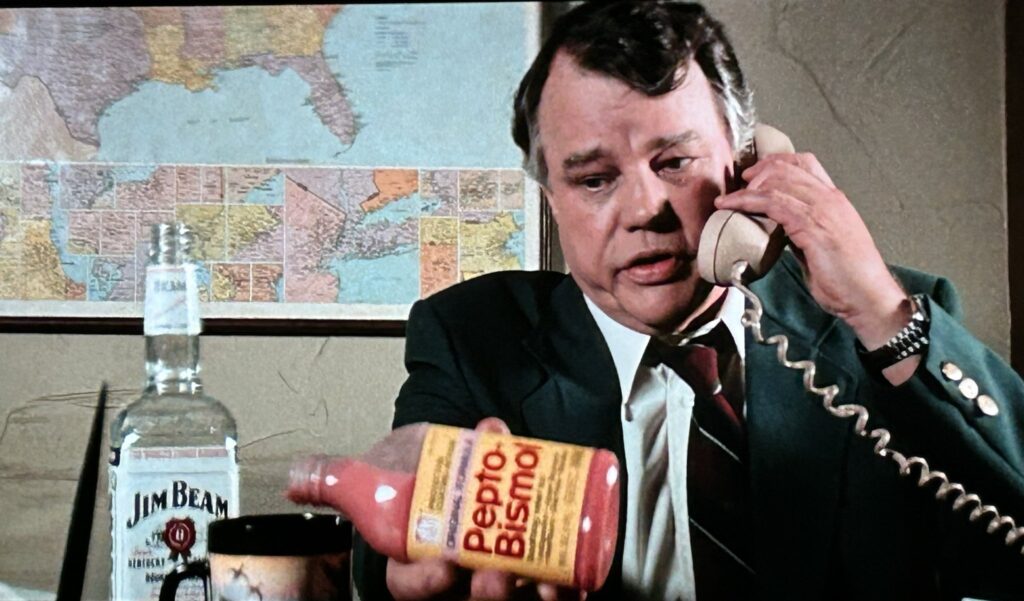 Joe Don Baker pouring Pepto-Bismol into a mug of whisky